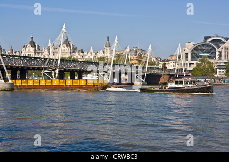 River Thames view with Hungerfiord Bridge and industrial boat pulling cargo freight container London England Europe Stock Photo