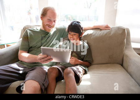 Father and adopted ten year old son watch a funny video on an Ipad at home. Father and adopted ten year old son watch a funny video on an Ipad at home.