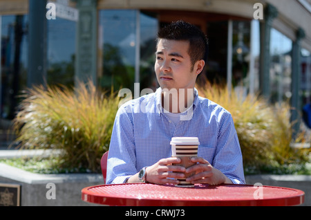 Young Asian man in a check shirt sitting outside with a hot drink Stock Photo