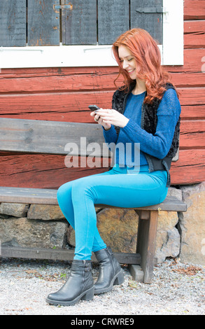 Pretty young lady with red hair using her smartphone and laughing Stock Photo