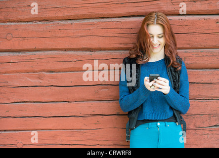 Young woman with red hair laughing and reading a text message on her phone Stock Photo