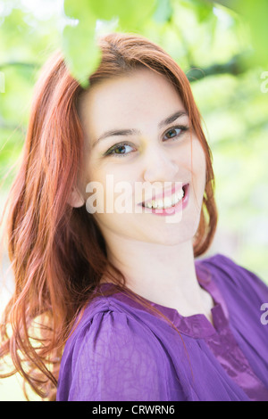 Happy young female adult with red hair in nature setting. Looking at camera and smiling. Stock Photo