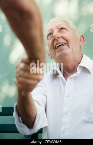 Active retirement, two old male friends talking and shaking hands on bench in public park Stock Photo