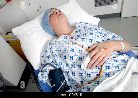 A female patient lies asleep, in a bed, wearing a pulse oximeter on her finger to monitor the oxygen content in her blood. Stock Photo