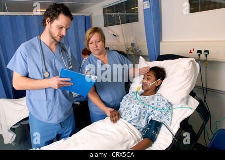 A doctor and a nurse on their ward rounds check the condition of a young woman patient wearing an oxygen mask. Stock Photo