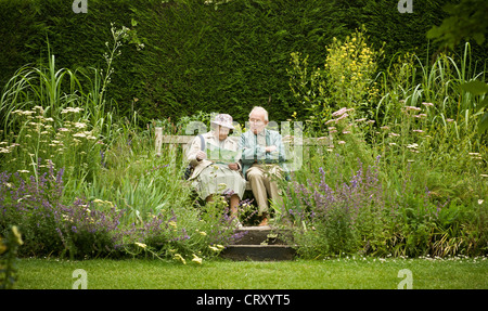 Elderly caucasian couple sat on wooden bench in garden looking at reading a leaflet Stock Photo