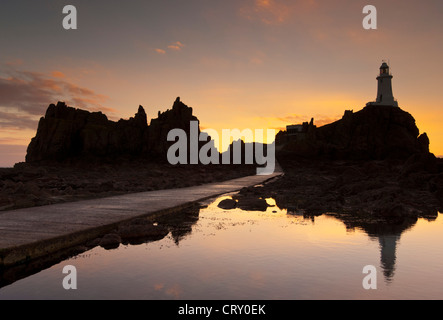 La Corbière Lighthouse sunset at Corbiere lighthouse and walkway uncovered at low tide Corbiere point Parish of St Brelade Jersey Channel Islands UK Stock Photo