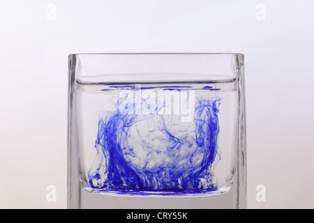 Blue ink swirls around in a glass of water Stock Photo