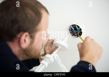 Electrician fixes new light fitting to ceiling fitting Stock Photo