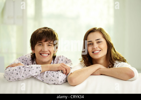 Young people leaning on their elbows on sofa and looking cheerfully at camera Stock Photo