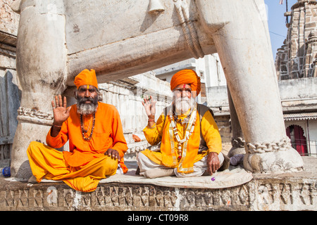 Two Sadhus, Indian Hindu holy men dressed in traditional saffron robes, sitting giving blessings begging for alms, Jagdish Temple, Udaipur, India Stock Photo