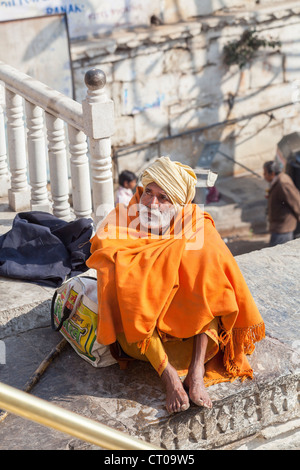 Sadhu, Indian Hindu holy man, wrapped in a traditional saffron shawl, sitting seeking alms at Jagdish Temple in Udaipur, Rajasthan, India Stock Photo