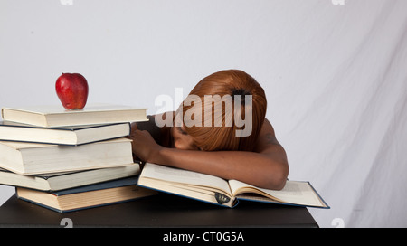 Female black student with a stack of books to study, and an apple on top, asleep on an open book. Studied too hard. Stock Photo
