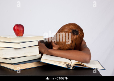 Female black student with a stack of books to study, and an apple on top, asleep on an open book. Studied too hard. Stock Photo
