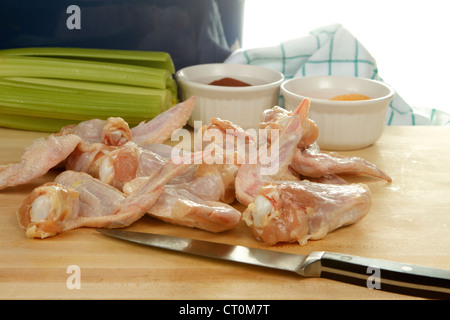 Raw Chicken wings being prepared for frying, on a wooded cutting board with celery and spices Stock Photo