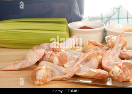 Raw Chicken wings being prepared for frying, on a wooded cutting board with celery and spices Stock Photo