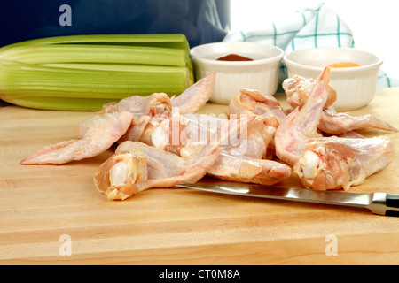 Raw Chicken wings being prepared for frying, on a wooded cutting board with celery and spices Stock Photo