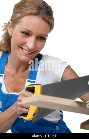 Woman wearing blue overalls sawing plank of wood Stock Photo