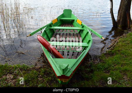 Rowing wooden boat near lake shore and red life saver resque circle in it. Stock Photo