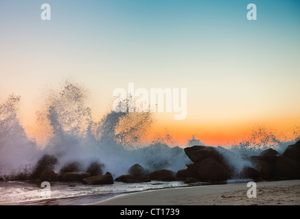 Waves crashing on rocky beach at sunset Stock Photo