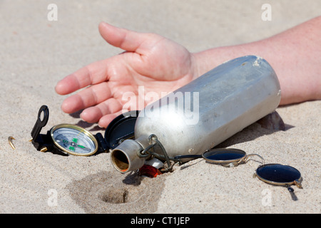 Human hand lies next to an empty canteen in the desert Stock Photo