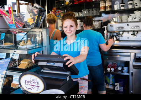 A happy smiling 14 fourteen year old girl working in a seaside refreshments cafe stall, UK  her weekend job while at school (MR) Stock Photo