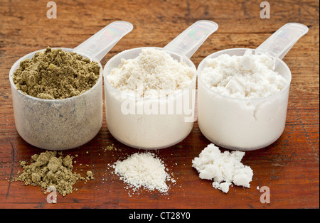 plastic measuring scoops of three protein powders (from left hemp seed, whey concentrate, whey isolate) on a grunge wood surface Stock Photo