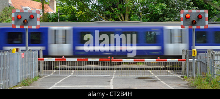 Railway tracks red flashing warning light sign level crossing barrier gates country road passenger train motion blur at Margaretting Essex England UK Stock Photo