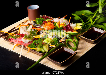 Mixed sashimi, raw fish with cucumber and seaweed on traditional japanese plate. soy sauce and chopsticks Stock Photo