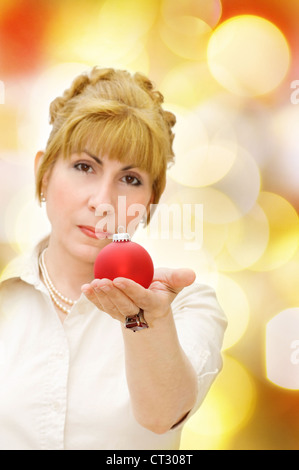 Merry Christmas! - woman giving red bauble. Over festive defocused lights. Stock Photo
