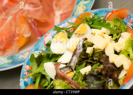 Fresh mixed salad with eggs, anchovies and arugula. Ham and melon on background. Stock Photo