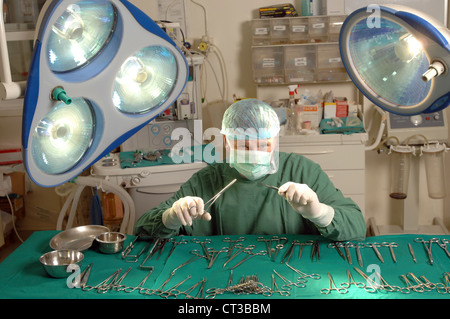 A surgeon in complete surgical dress brandishing surgical tools in an operating theatre. Stock Photo