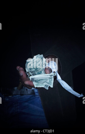 Hand holding wadded dollar bills in dark Stock Photo