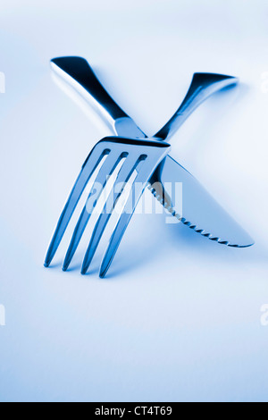 Crossed over blue tone knife and fork with space for text. Stock Photo