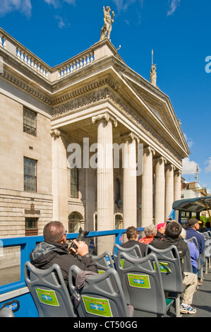 Tourists on top of a 'hop on hop off' city tour bus drive past the General Post Office on O'Connell Street. Stock Photo