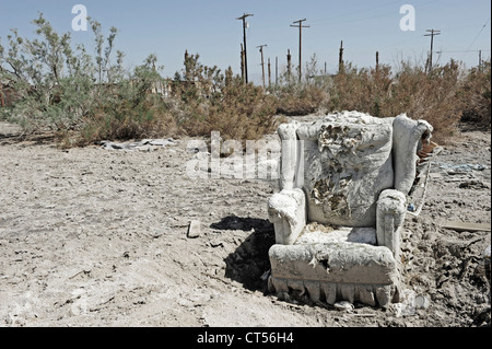 An abandoned chair, Salton Sea Beach, Southern California, USA. Ripped upholstered chair on scrub land, telegraph poles behind. Stock Photo
