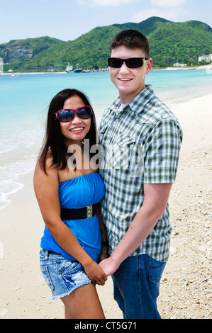 Young adult mixed race couple holds hands and smiles for the camera on a beautiful beach in Okinawa, Japan. Stock Photo