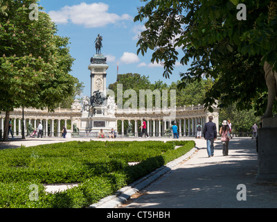 Couple walking along Paseo de Argentina towards statue of King Alfonso XII in Retiro Park, Madrid Stock Photo