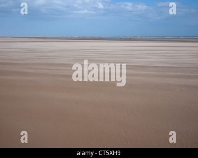 a view of Camber Sands on a windy day with sand blowing across the beach with blue sky Stock Photo
