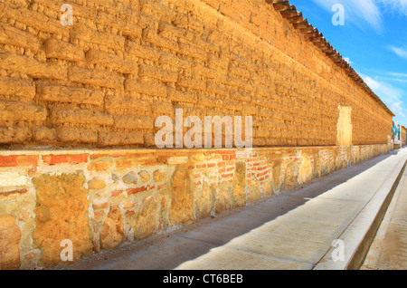 Long Adobe brick wall in weathered state vanishing into distant point on horizon with blue sky. Sunny day. Stock Photo