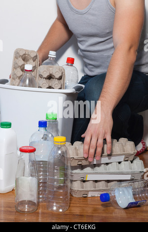 Young man putting egg carton and plastic bottles in recycling bin Stock Photo