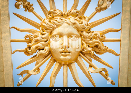 Detail view of golden ornate gate of Chateau de Versailles depicting human face. Blue sky in background. Paris, France, Europe. Stock Photo