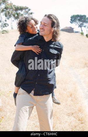 Father is piggy backing son in a field. Stock Photo