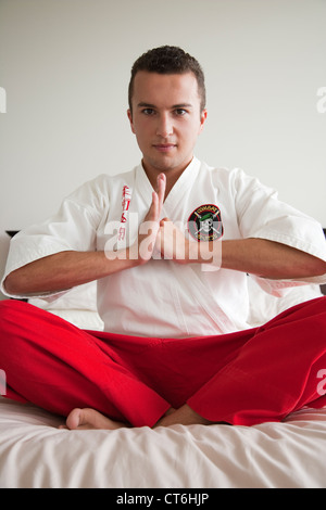 Portrait of a confident young man sitting in kung fu position on bed Stock Photo