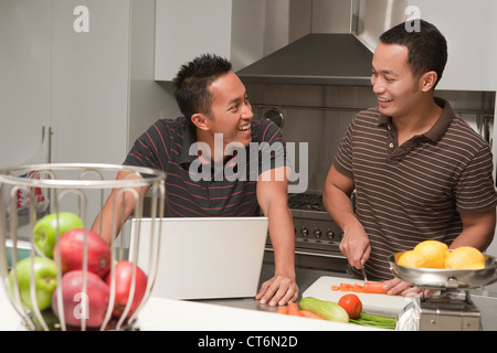 Happy homosexual couple using laptop while preparing food in kitchen Stock Photo