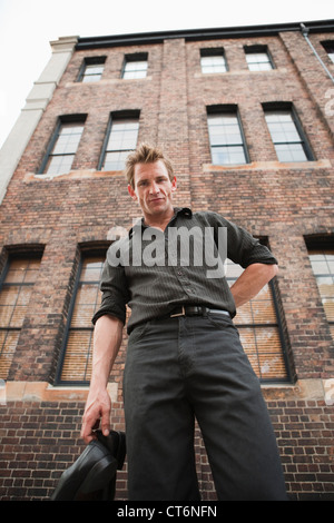 Portrait of a handsome young man holding his shoes in front of a building Stock Photo