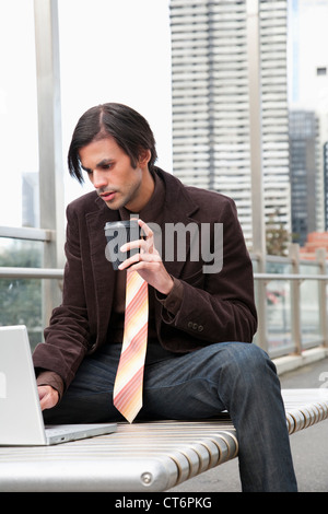 Businessman using laptop and holding disposable cup Stock Photo
