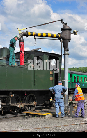 Engine driver and crew filling boiler of steam train from water crane ...