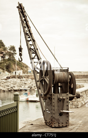Old fishing crane in small seaside town harbor. Toned image Stock Photo
