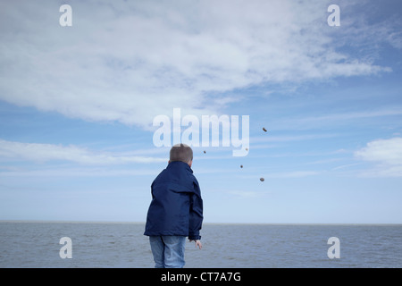 Little boy throwing stones into the sea Stock Photo